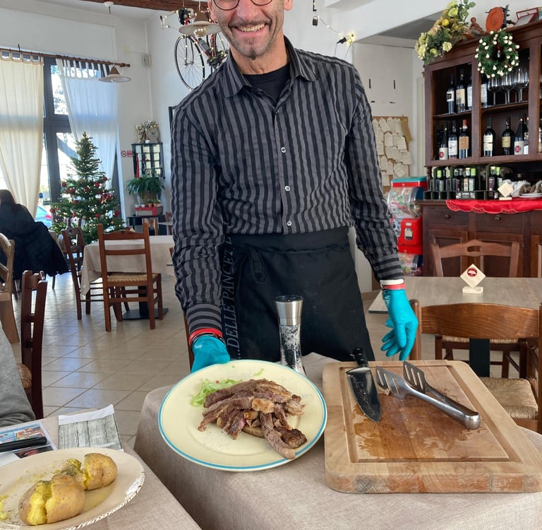 Smiling waiter serving a sliced steak platter in a cozy Italian restaurant with festive decor.