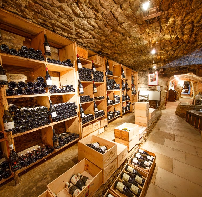 Rustic underground wine cellar with stone walls and wooden shelves storing vintage wine bottles.