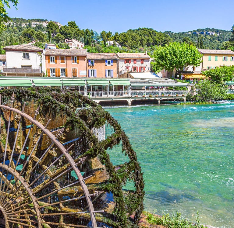 A moss-covered antique water wheel turns in the Sorgue River near waterfront cafes in Fontaine-de-Vaucluse, France.