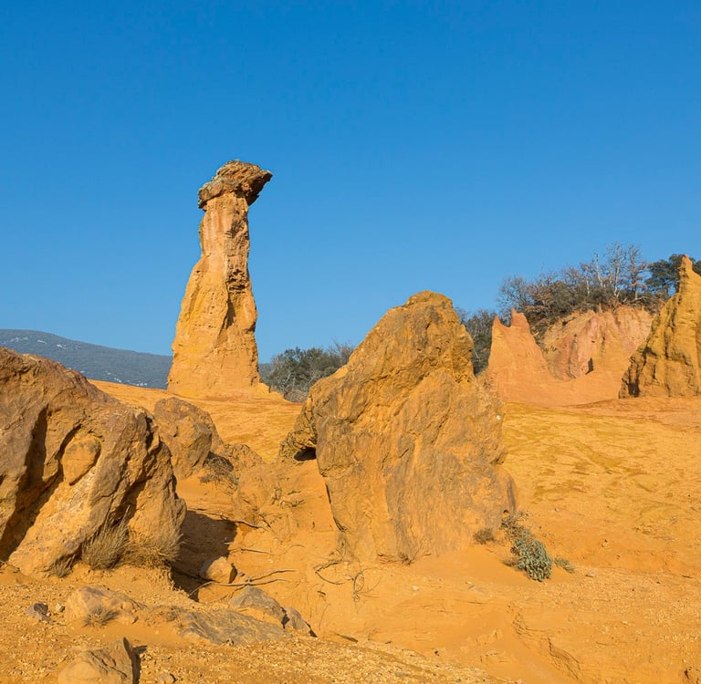 Tall orange ochre rock formation at Colorado Provençal in Rustrel, France, under a clear blue sky.