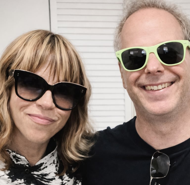 Tracy and Dan wearing stylish sunglasses and casual attire standing together.