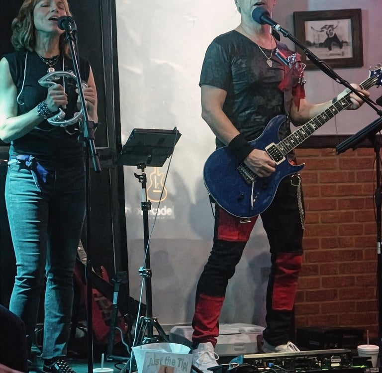Live band performance featuring a female singer with a tambourine and a male guitarist on stage.