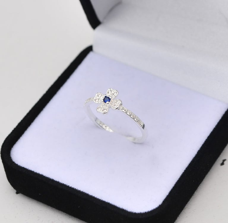 Sterling silver four-leaf clover ring with blue sapphire center in a black velvet jewelry box.
