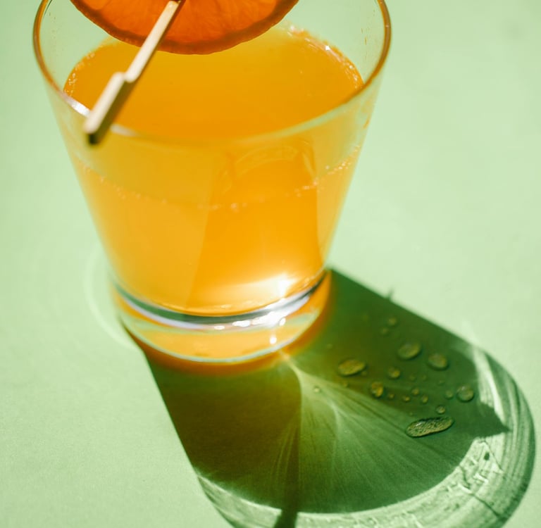 A clear glass filled with bright orange liquid on a light green surface