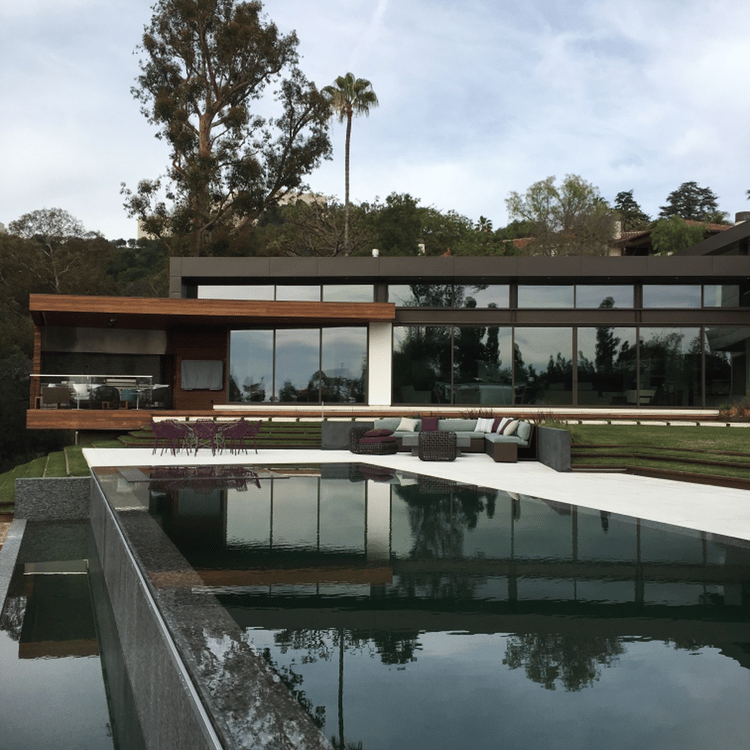 a vanishing edge pool and spa with a view of a large house