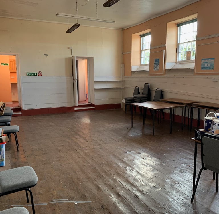 Former school hall with worn wooden floors and original windows before renovation