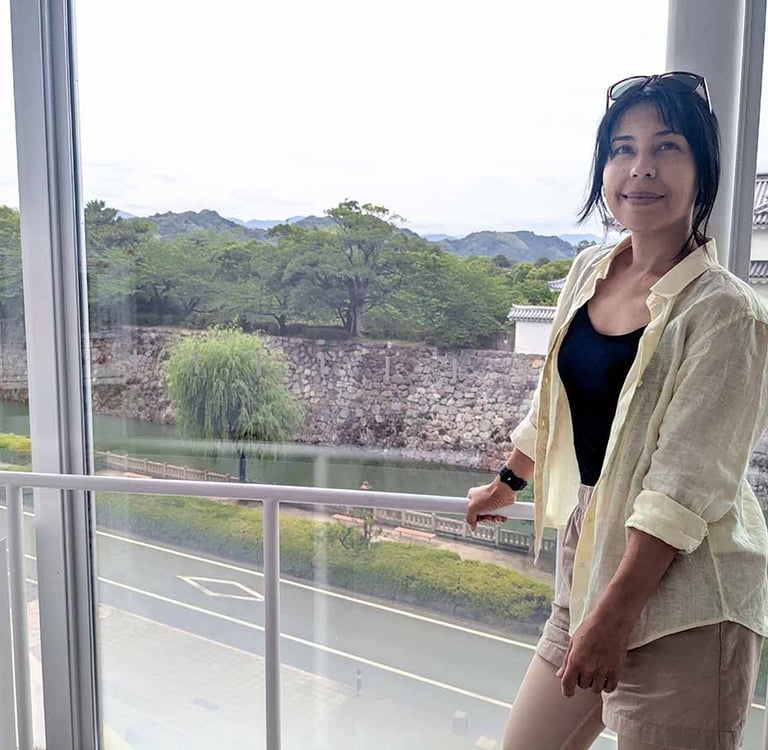 Woman standing beside a large window overlooking Sunpu Castle and its moat in Shizuoka.