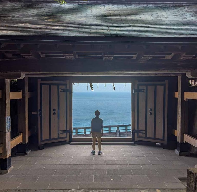 Silhouette of a woman framed by a temple gate with ocean views beyond in Shizuoka, Japan.