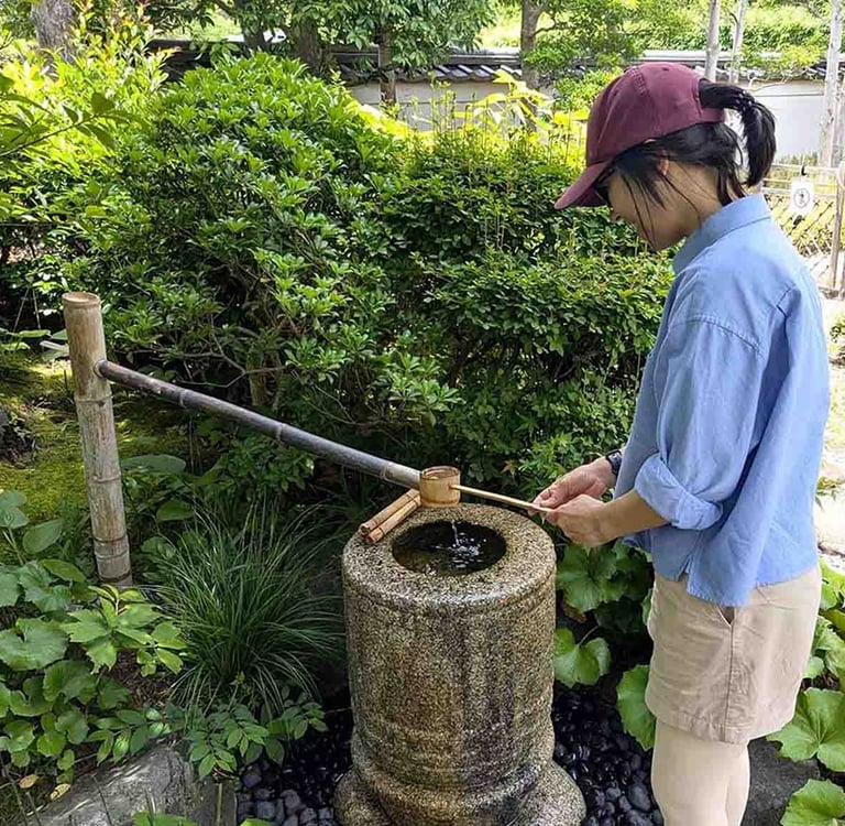 Woman using a traditional stone water basin in a Japanese garden.