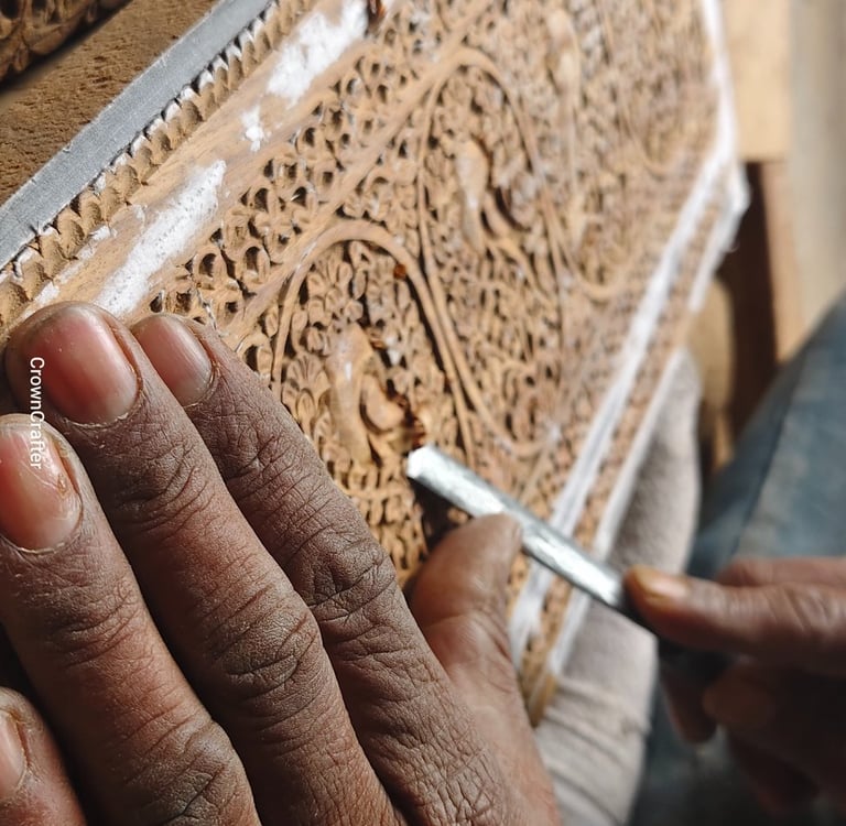 Artisan hand carving intricate floral patterns into a wooden panel using a traditional metal chisel.