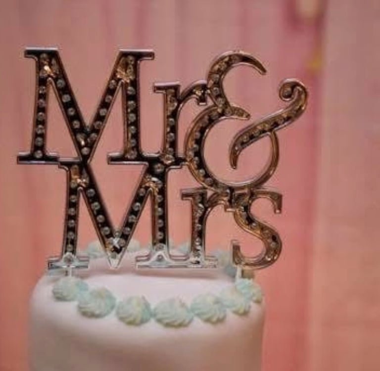 Elegant silver Mr & Mrs wedding cake topper with sparkling crystals on a white tiered cake.