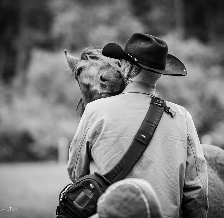 A black and white photo showing Drake in a cowboy hat sharing an affectionate moment with a horse. 