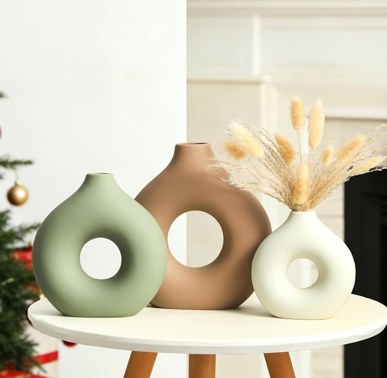 Set of three modern ceramic donut vases in sage green, tan, and white on a side table.