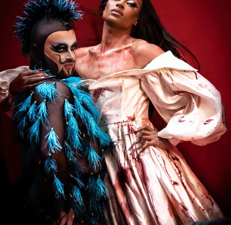 Two drag performers in artistic makeup and high-fashion horror costumes pose against a red background.