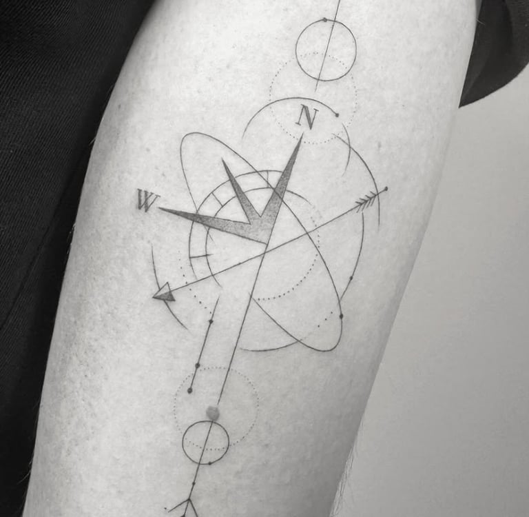 Tatuaje fineline brújula geométrica con átomo y flechas en antebrazo madrid