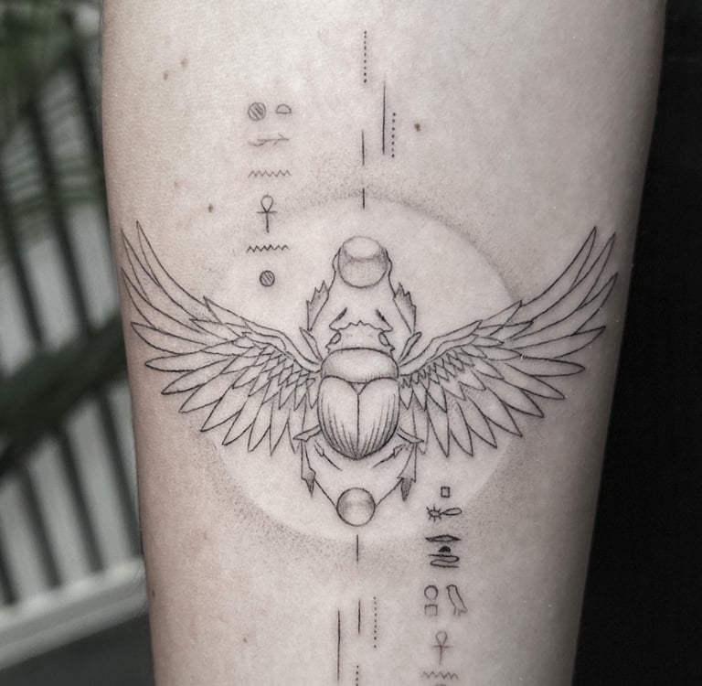Tatuaje fineline escarabajo egipcio alado con jeroglíficos en antebrazo madrid