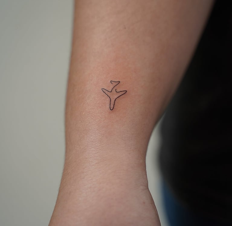 Tatuaje fineline en Madrid de avión pequeño en trazo continuo y minimalista en el antebrazo