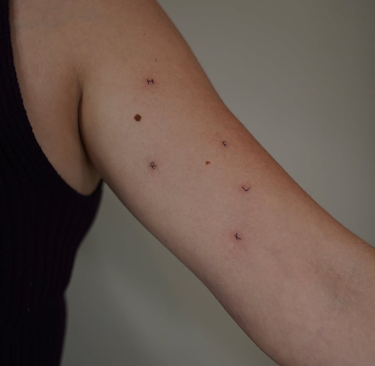 Tatuaje fineline en Madrid de iniciales H F C L K dispersas en trazo fino en el brazo