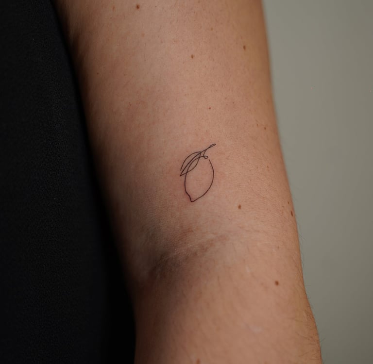 Tatuaje fineline en Madrid de limón minimalista en trazo fino con hoja en el antebrazo