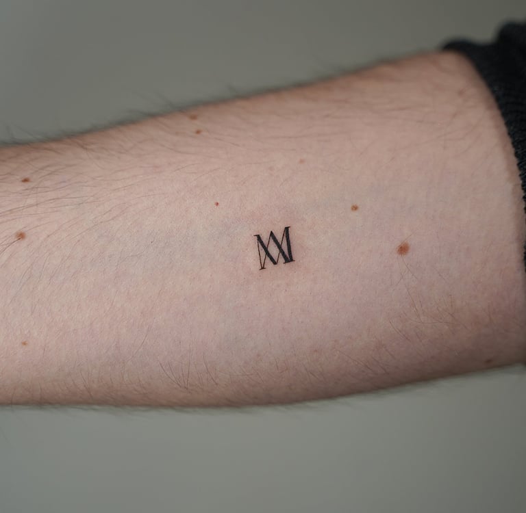 Tatuaje fineline en Madrid de iniciales MM en tipografía serif elegante en el antebrazo
