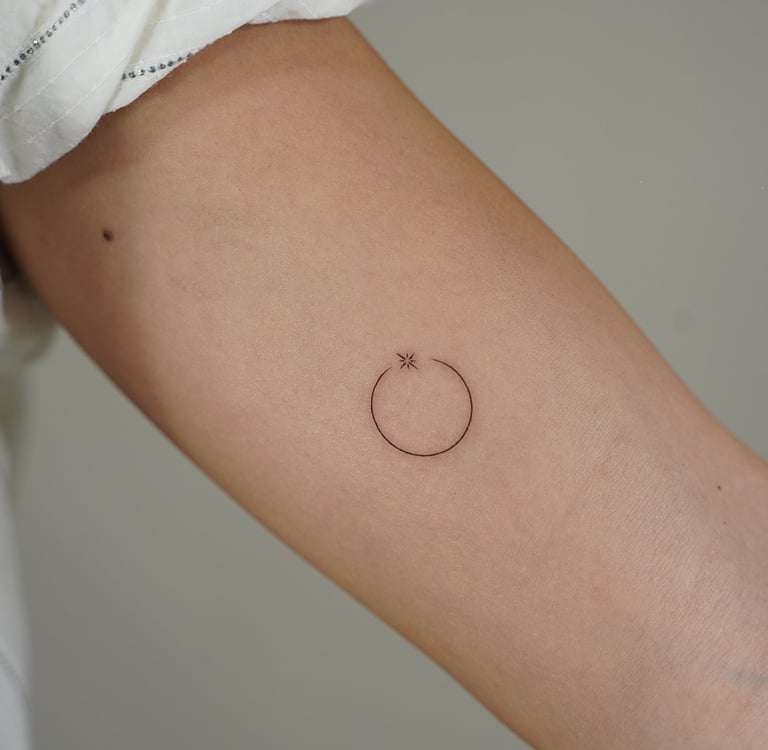 Tatuaje fineline en Madrid de círculo minimalista con estrella pequeña en trazo fino en el antebrazo