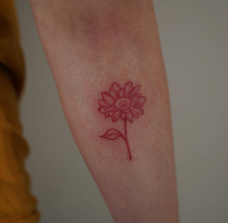 Tatuaje fineline en Madrid de girasol botánico en tinta roja con pétalos detallados