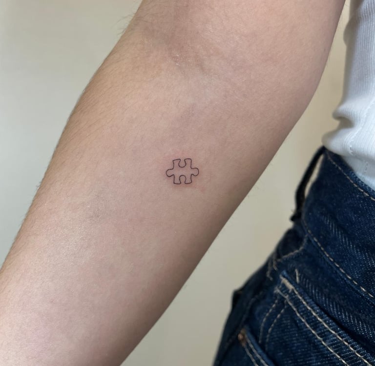 Tatuaje fineline en Madrid de pieza de puzzle en trazo fino y minimalista en el antebrazo