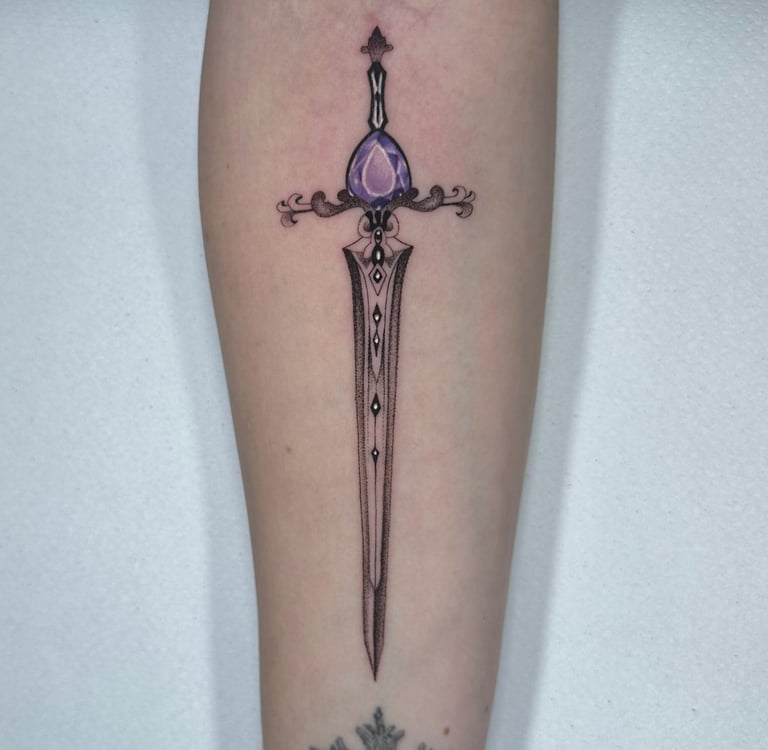 Tatuaje fineline en Madrid de espada ornamental con gema morada empuñadura decorada