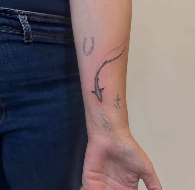 Tatuaje fineline en Madrid de tiburón realista en movimiento con herradura y nombre en cursiva