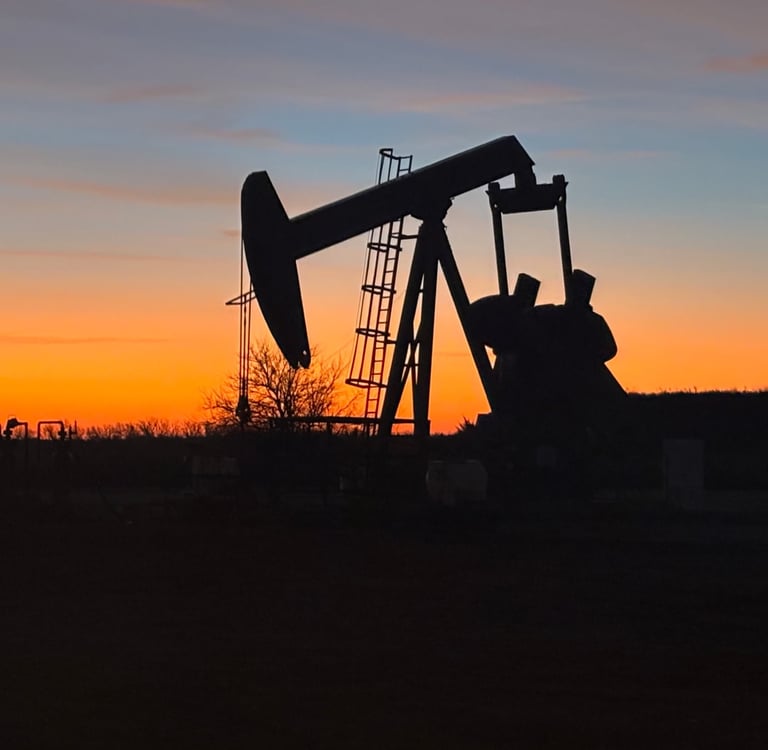 Silhouette of an oil pump jack extraction rig operating against a vibrant orange sunset horizon.