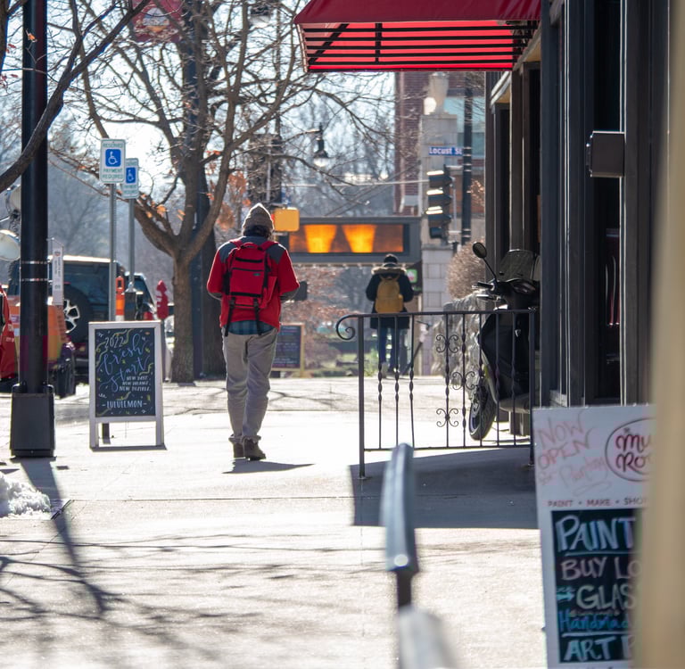 Man walking on a sidewalk downtown past business and sandwich signs