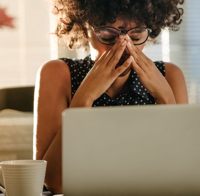 A person looking stressed and overwhelmed while working at a laptop with multiple open tabs and a coffee cup