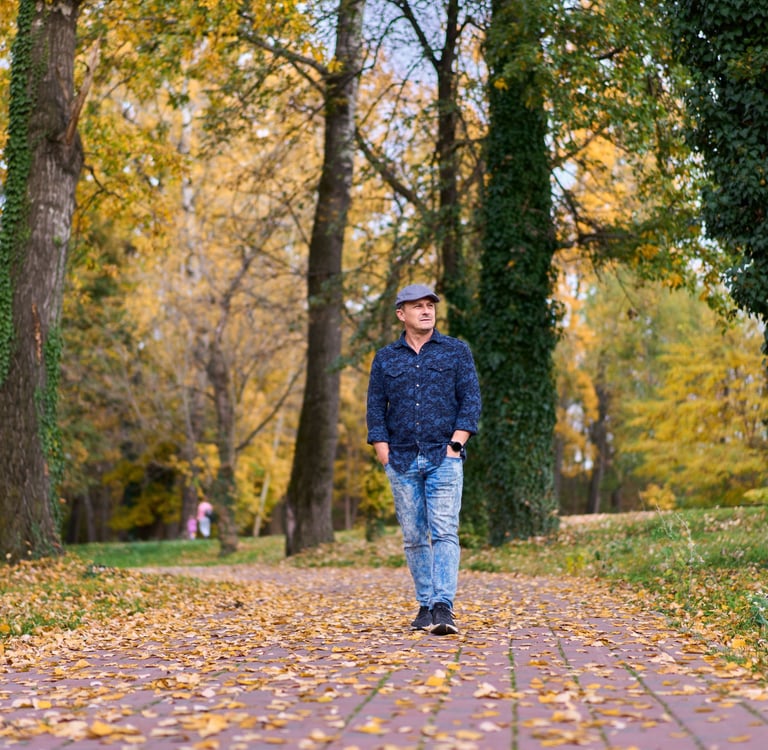 A man walking along a paved path in a Calgary park on a fall afternoon, hands in jacket pockets, contemplative expression