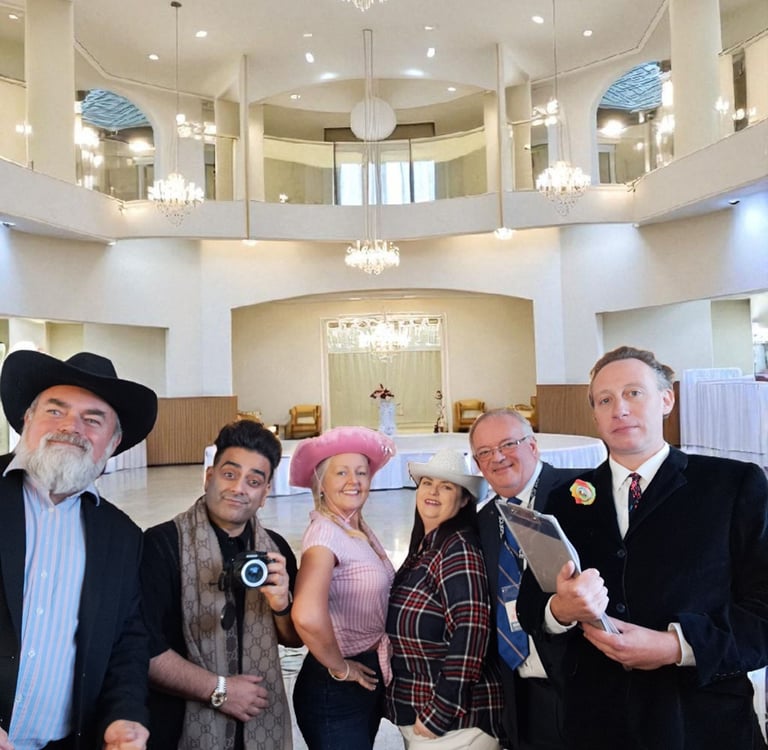 Diverse group of event professionals wearing cowboy hats posing in a grand ballroom with chandeliers.