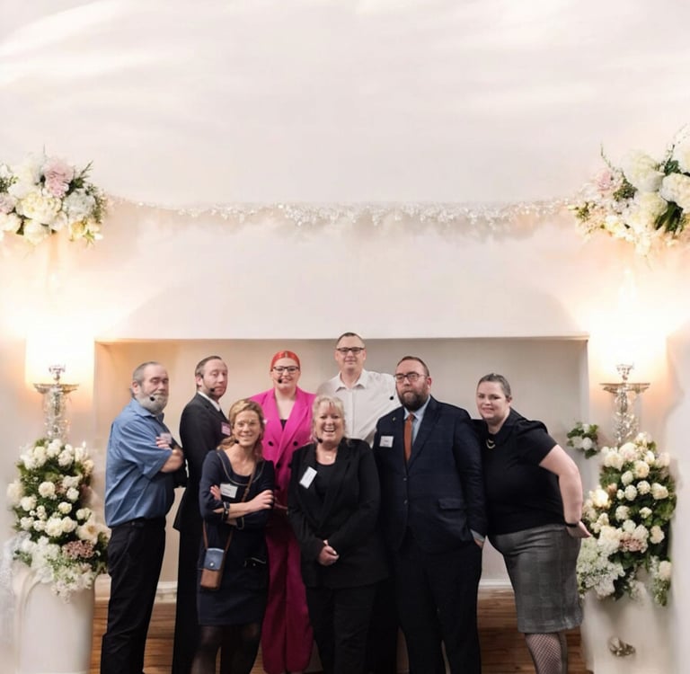 A group of professionals posing together at a business event with floral decorations and warm lighting.