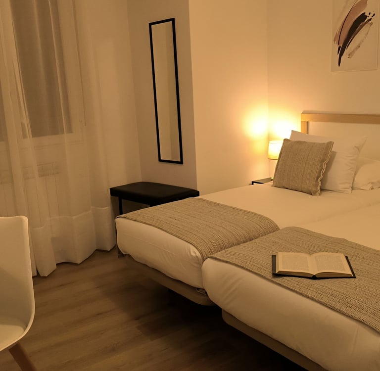 Habitación con camas gemelas en hotel Arias, Vigo, con espejo, ventana y lampara encendida