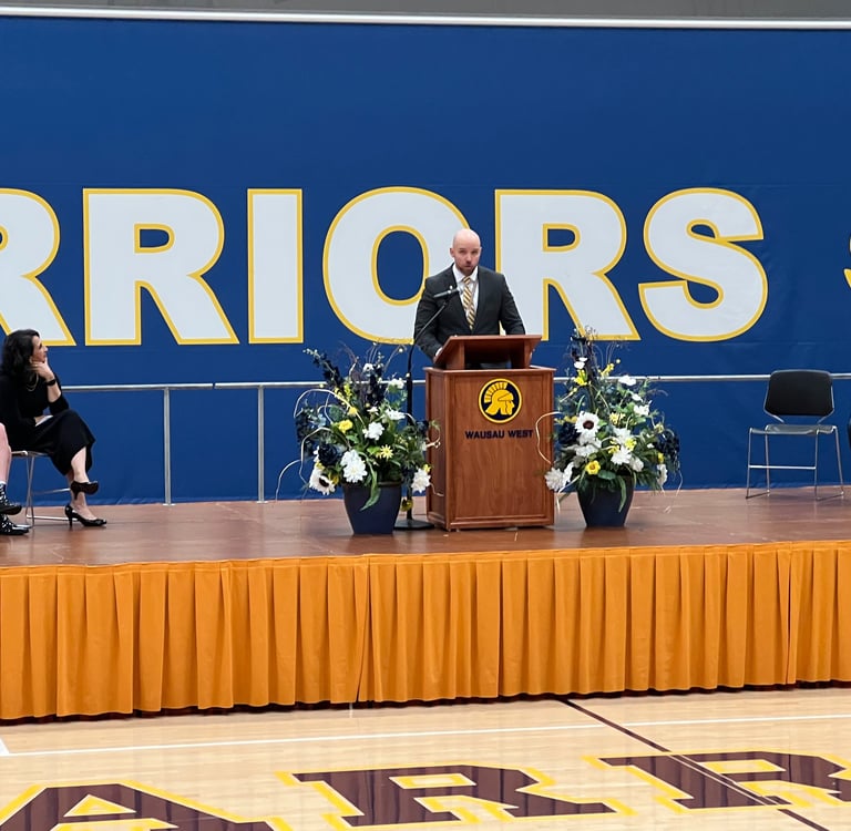 a man standing at a podium with a microphone and a woman sitting at a podium