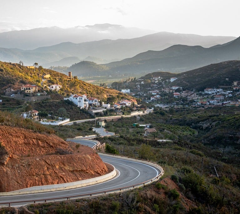 Winding road leading towards a Spanish mountain village and fading mountains in the background