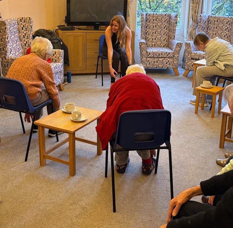 Group of elderly residents taking part in a seated exercise and chair yoga class, led by Lucy