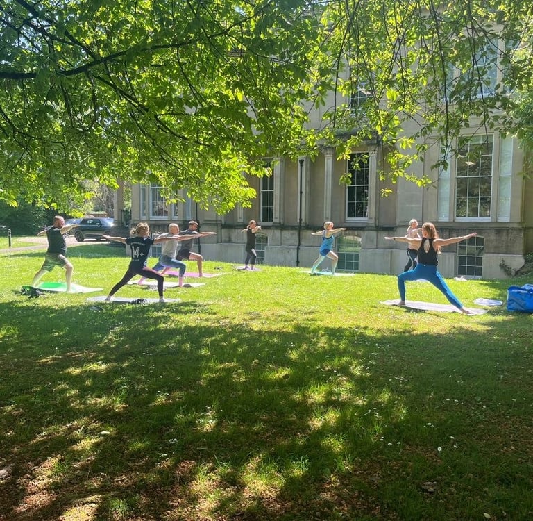 Outdoor yoga class practising poses on grass in a park.
