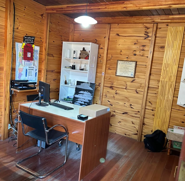 Despacho rústico en oficina con escritorio de madera y ordenador, con paredes revestidas en madera.