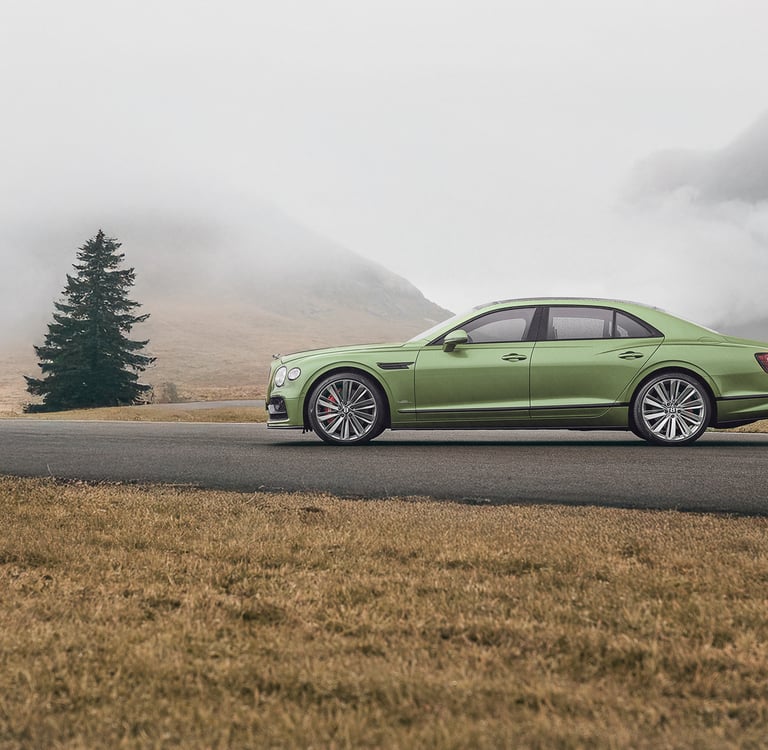 a green bentley driving down a road with a mountain in the background