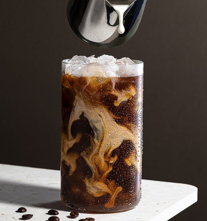 a glass of iced coffee with a pitcher of milk