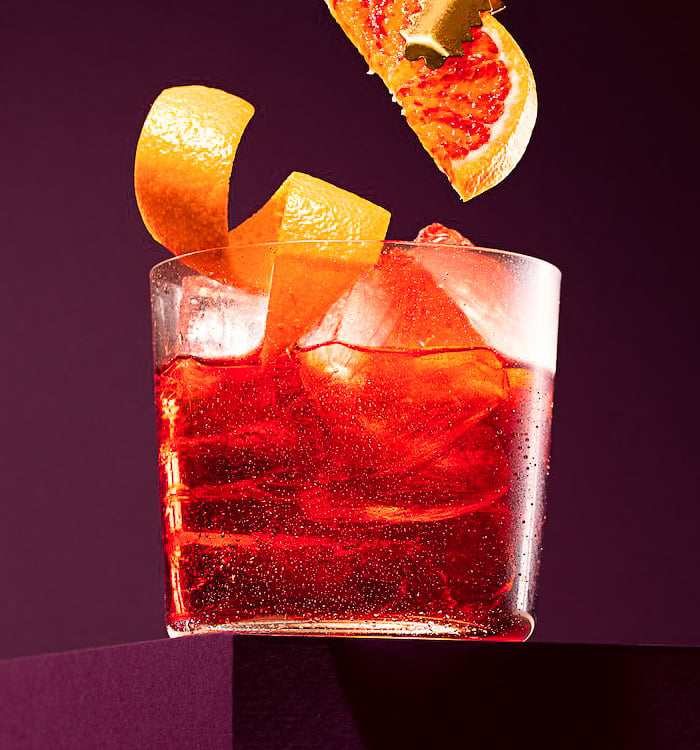 a glass of red wine with a slice of orange peel on top of it