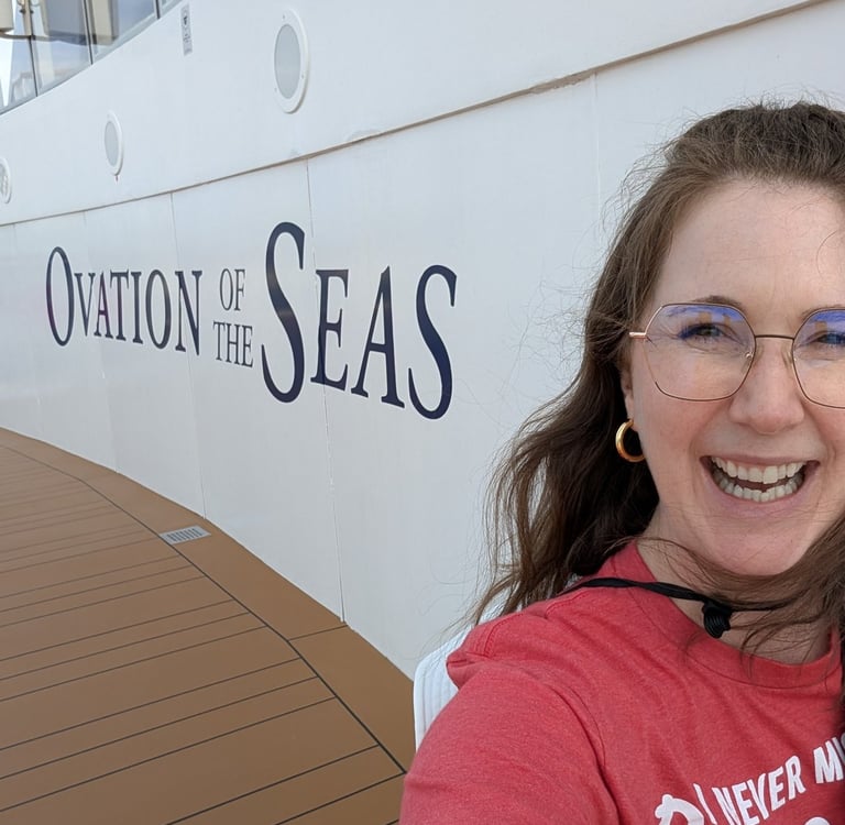 A woman smiling by the side of a Royal Caribbean ship that says Ovation of the Seas
