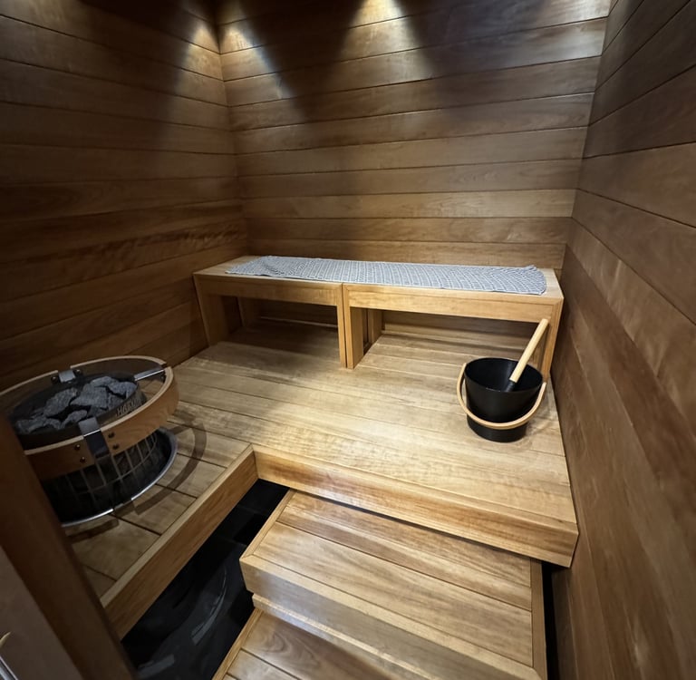 Modern wood sauna interior with tiered benches, electric heater, and bucket accessory