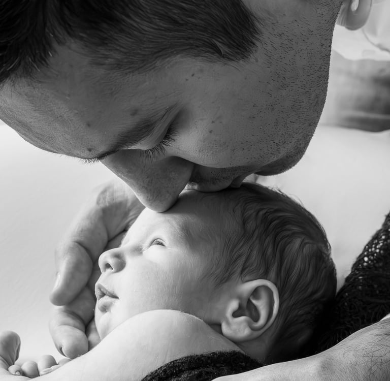 Black and white close-up of a father kissing his newborn baby on the forehead during a lifestyle photography session.