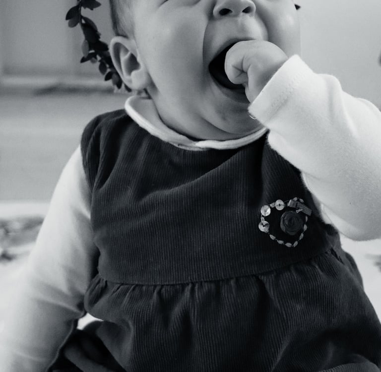 Black and white portrait of a happy baby girl wearing a floral headband and corduroy dress.
