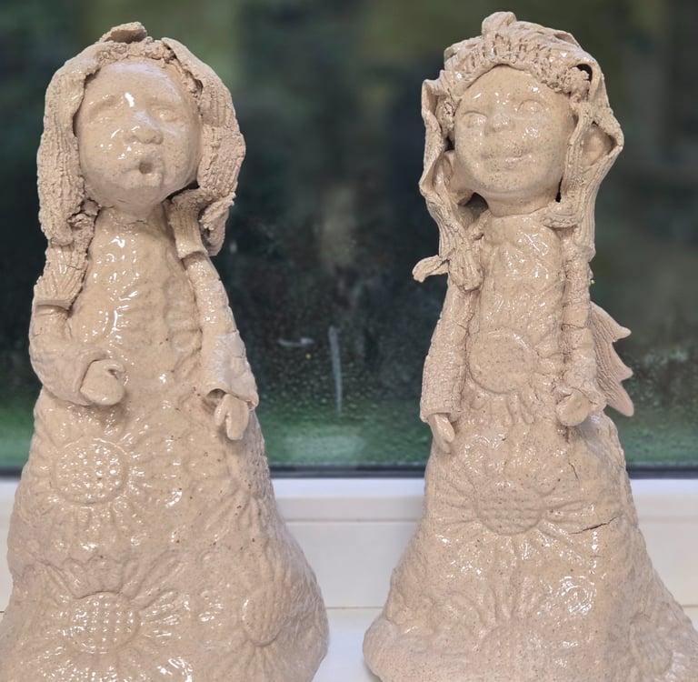 Two handmade ceramic angel figurines with glazed finishes on a windowsill.