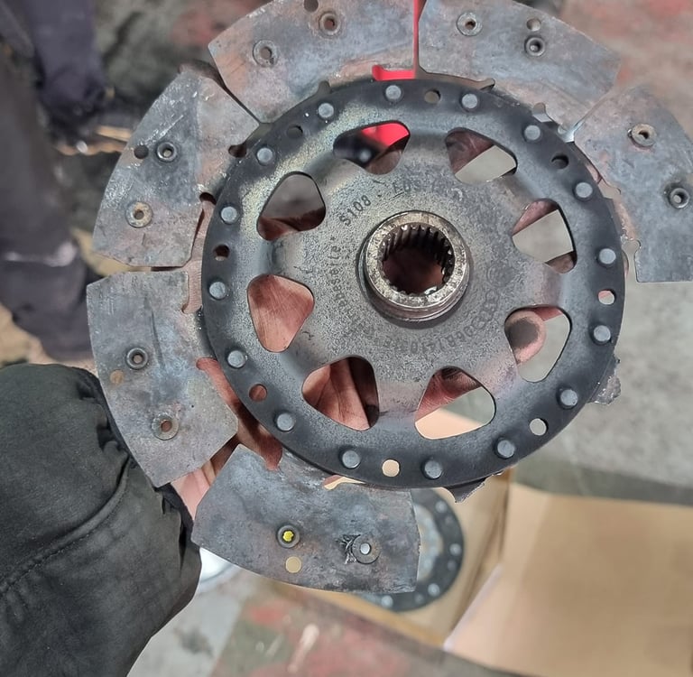 A mechanic holding a worn and damaged automotive clutch friction disc in a repair shop.